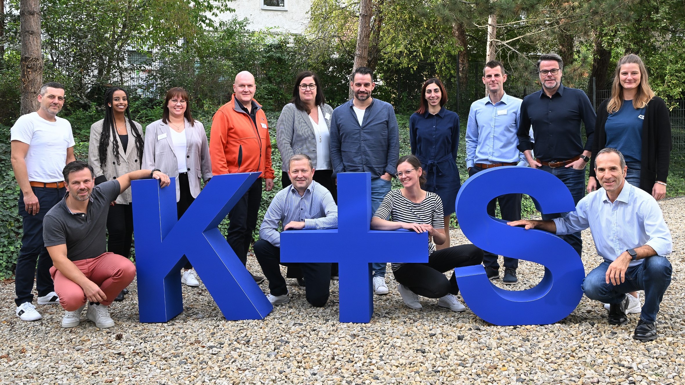 Gruppenfoto von 14 Mitarbeiter:innen der Kpluss AG hinter großen blauen kpluss Buchstaben 