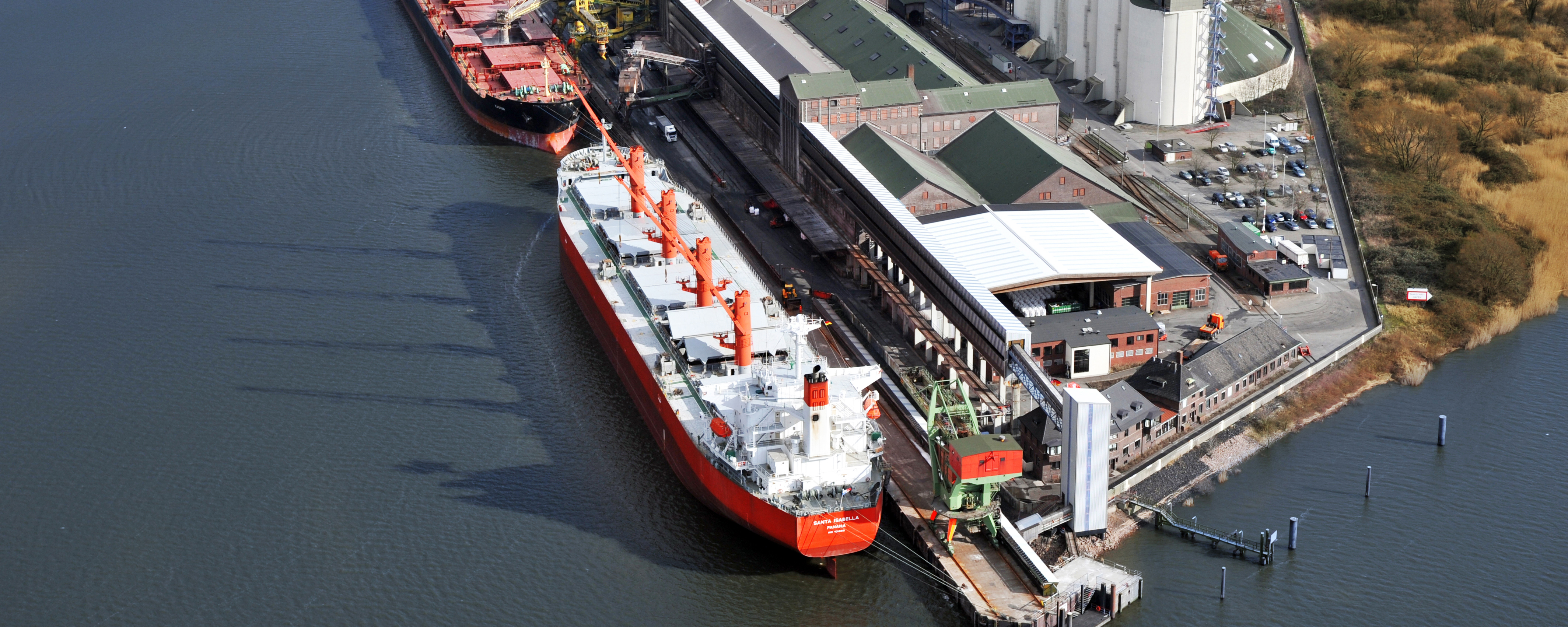 Vogelperspektive des K+S Standorts Hamburg Kalikai im Hamburger Hafen. Im Vordergrund sind zwei Binnenschiffe zu sehen. Dahinter ist der Hafenbetrieb zu sehen. 