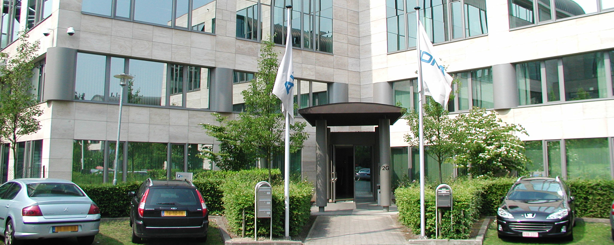 Frontalansicht des Firmensitz der K+S Benelux. Das Firmengebäude ist weiß und besitzt große Glasfenster und einem grün bepflanzten Vorgarten. Vor dem Gebäude ist ein Parkplatz.