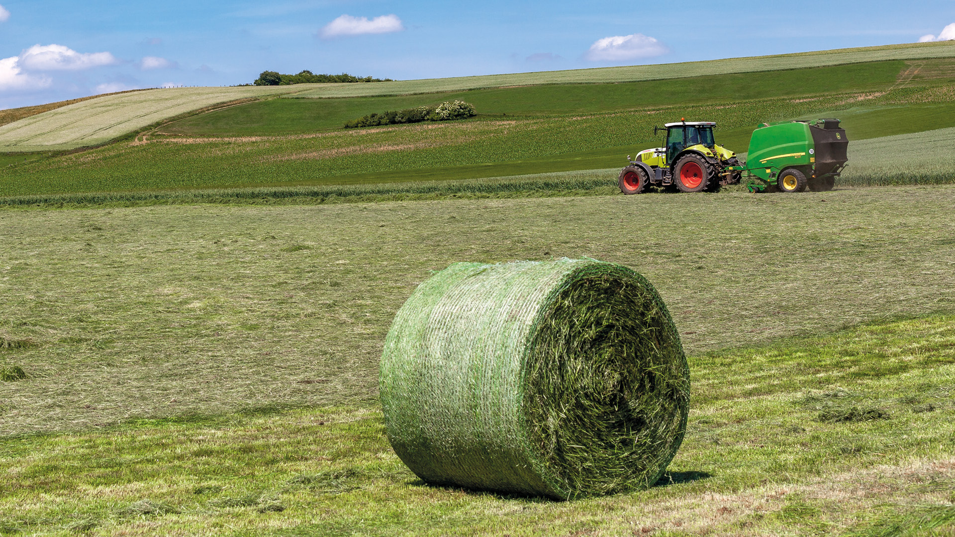Auf der linken Seite des Bildes ist das Logo der KALI Akademie zu sehen. Auf der rechten Seite sieht man einen Heuballen und im Hintergrund fährt ein Traktor.