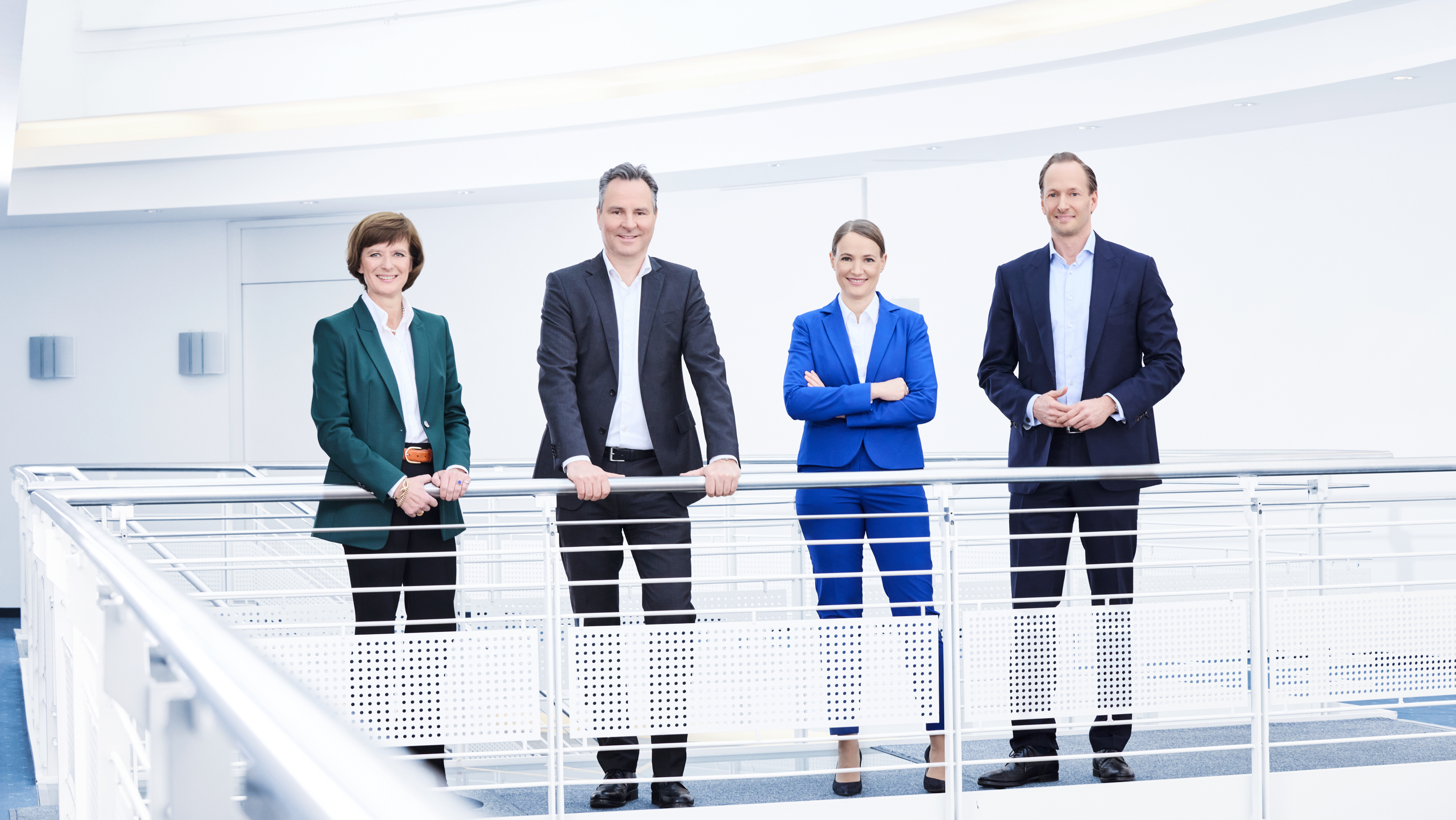 The four K+S Executive Board members Dr. Carin-Martina Tröltzsch, Dr. Christian Meyer, Christina Daske and Dr. Jens Christian Keuthen stand on a pedestal in a bright stairwell and smile friendly into the camera.