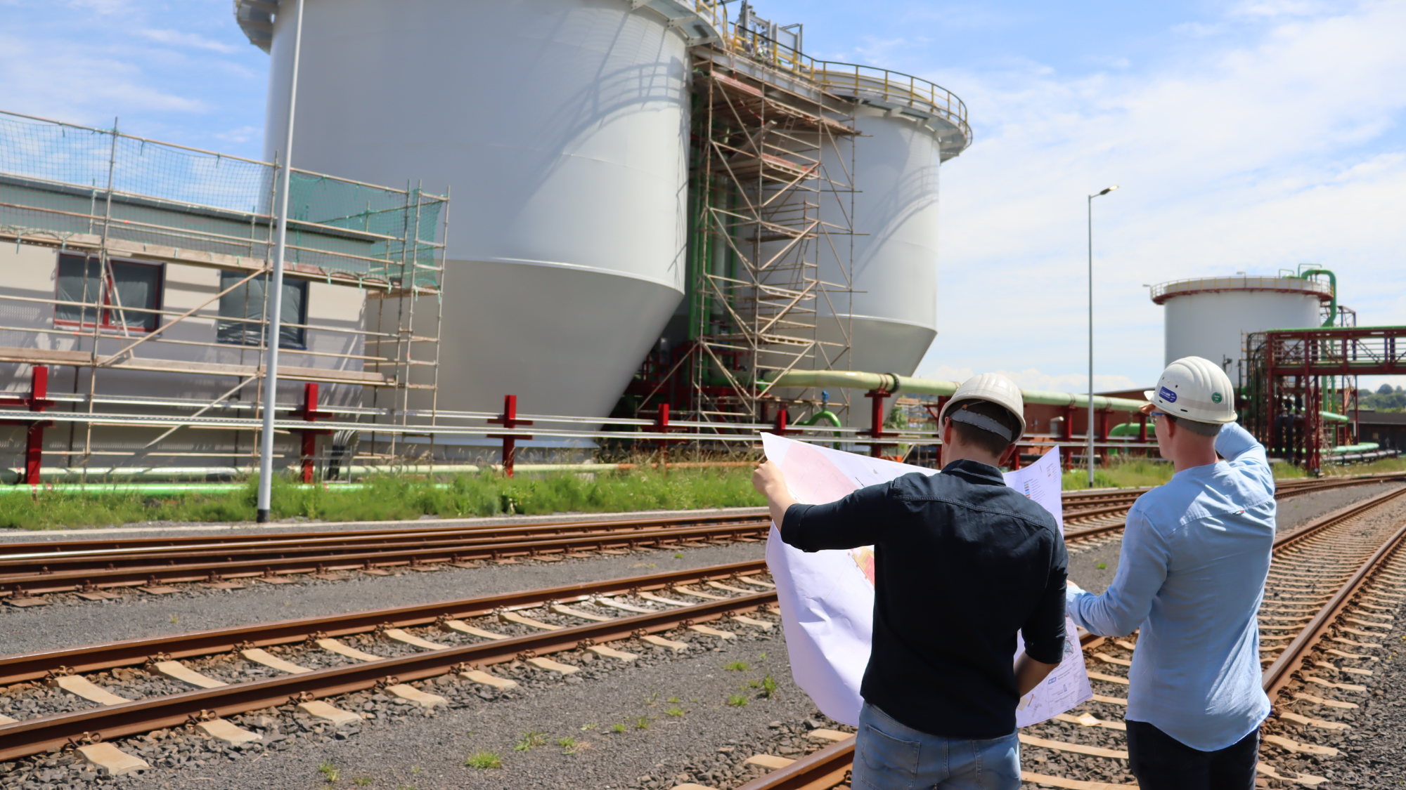 Zwei Maschinenbau-Studierende mit Bauhelmen vor Industrieanlage.