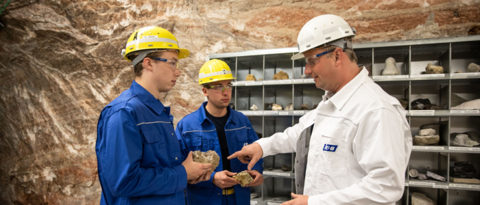 Drei Mitarbeiter in Arbeitskleidung schauen sich Salzkristalle an.