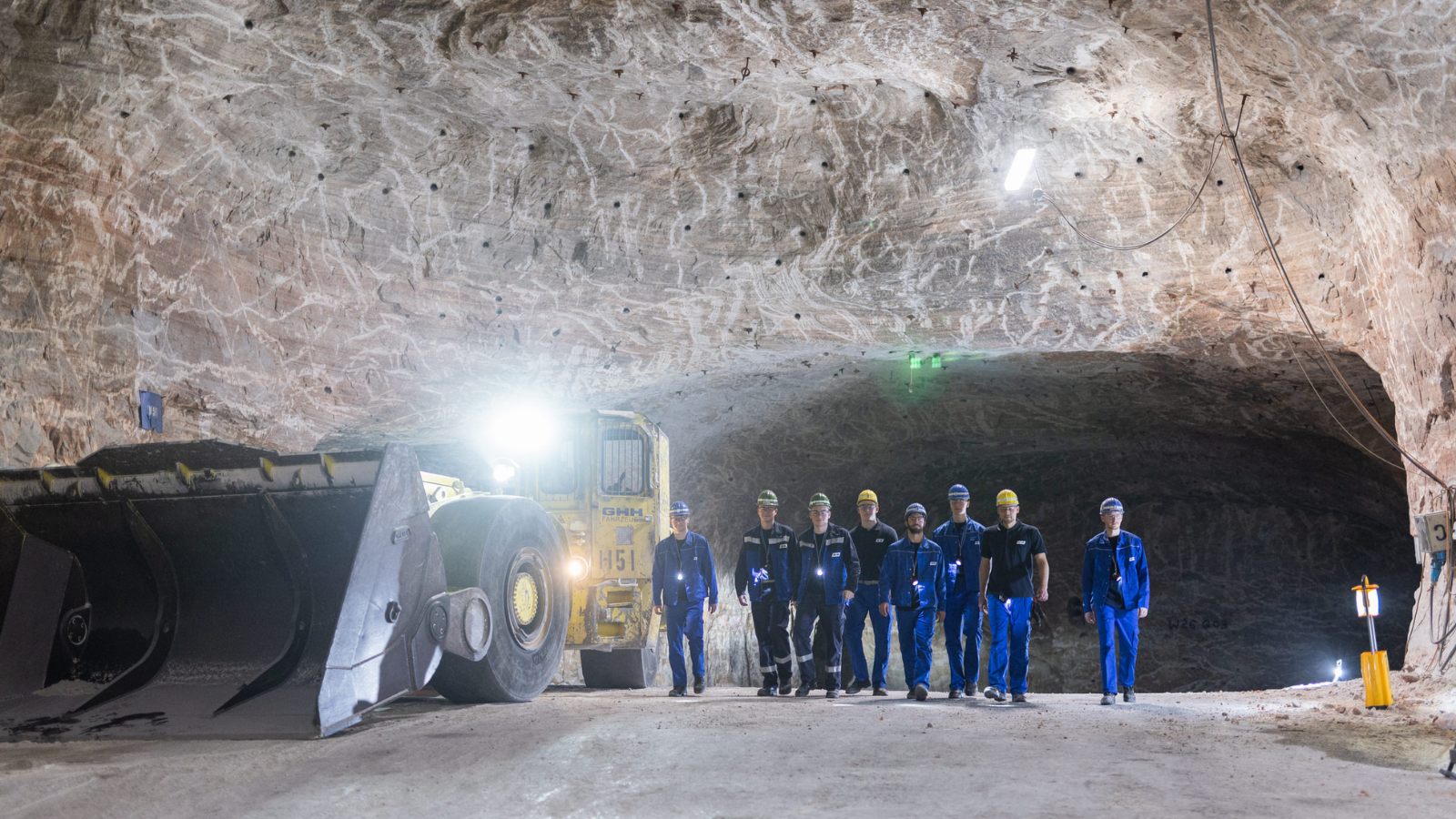 Mitarbeitende gehen unter Tage auf die Kamera zu, begleitet von einem großen Lader.