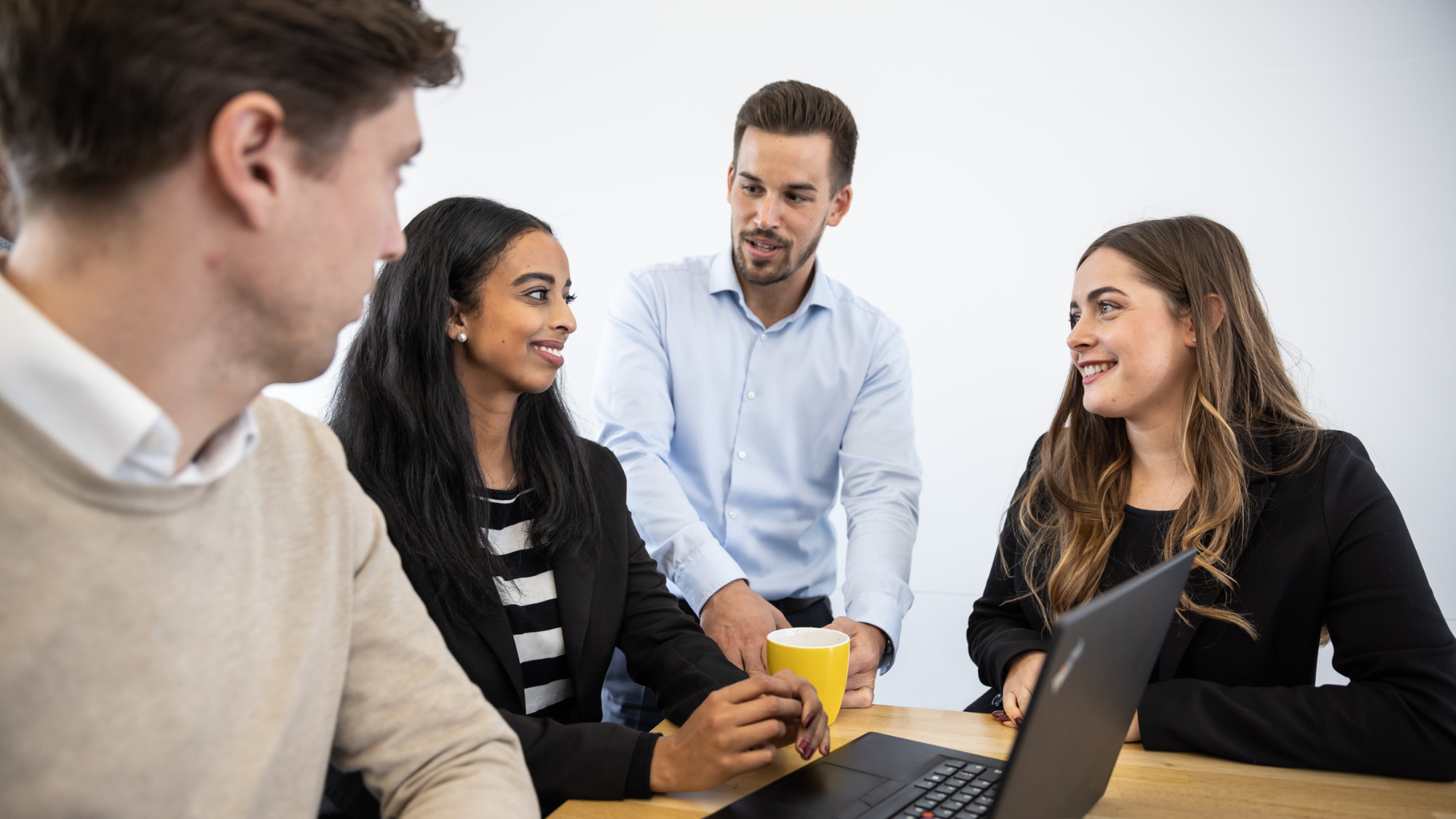 Kolleg:innen im Austausch an einem Tisch mit Laptop