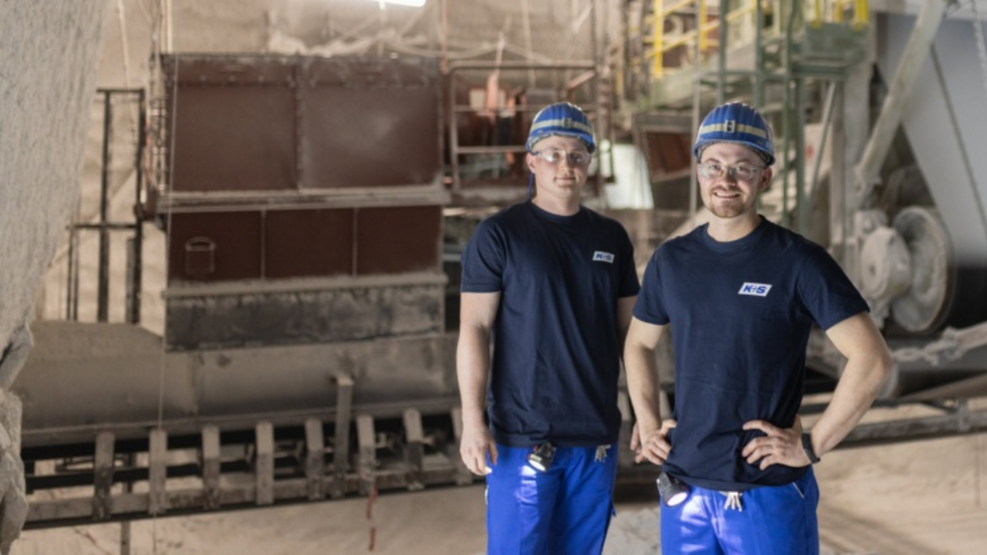 Zwei Mitarbeiter vor einer Anlage, unter Tage. 