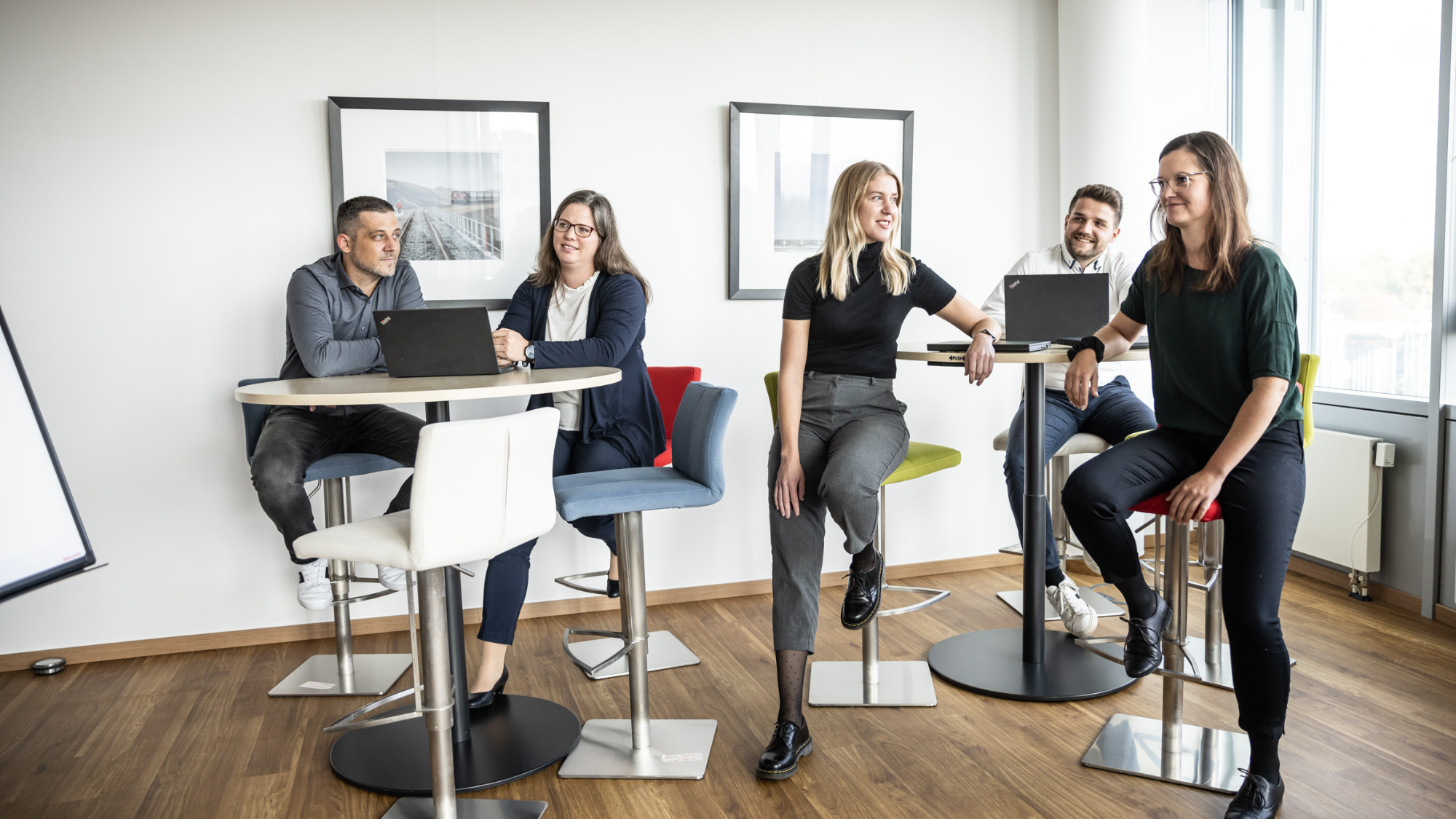 Five employees are standing at a high table, talking to each other.