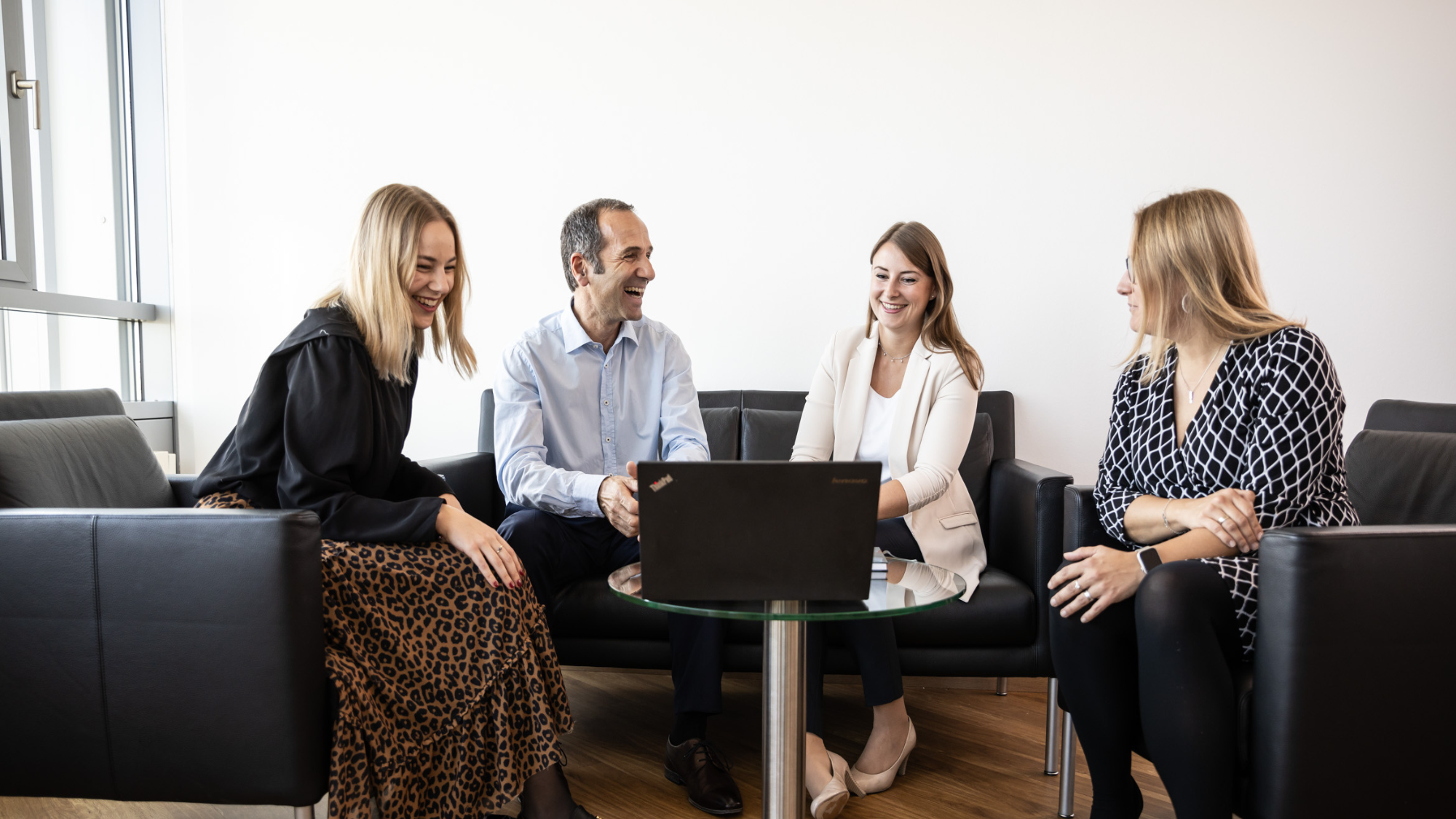 Vier Mitarbeiter und Mitarbeiterinnen sitzen auf der Couch vor einem Laptop.