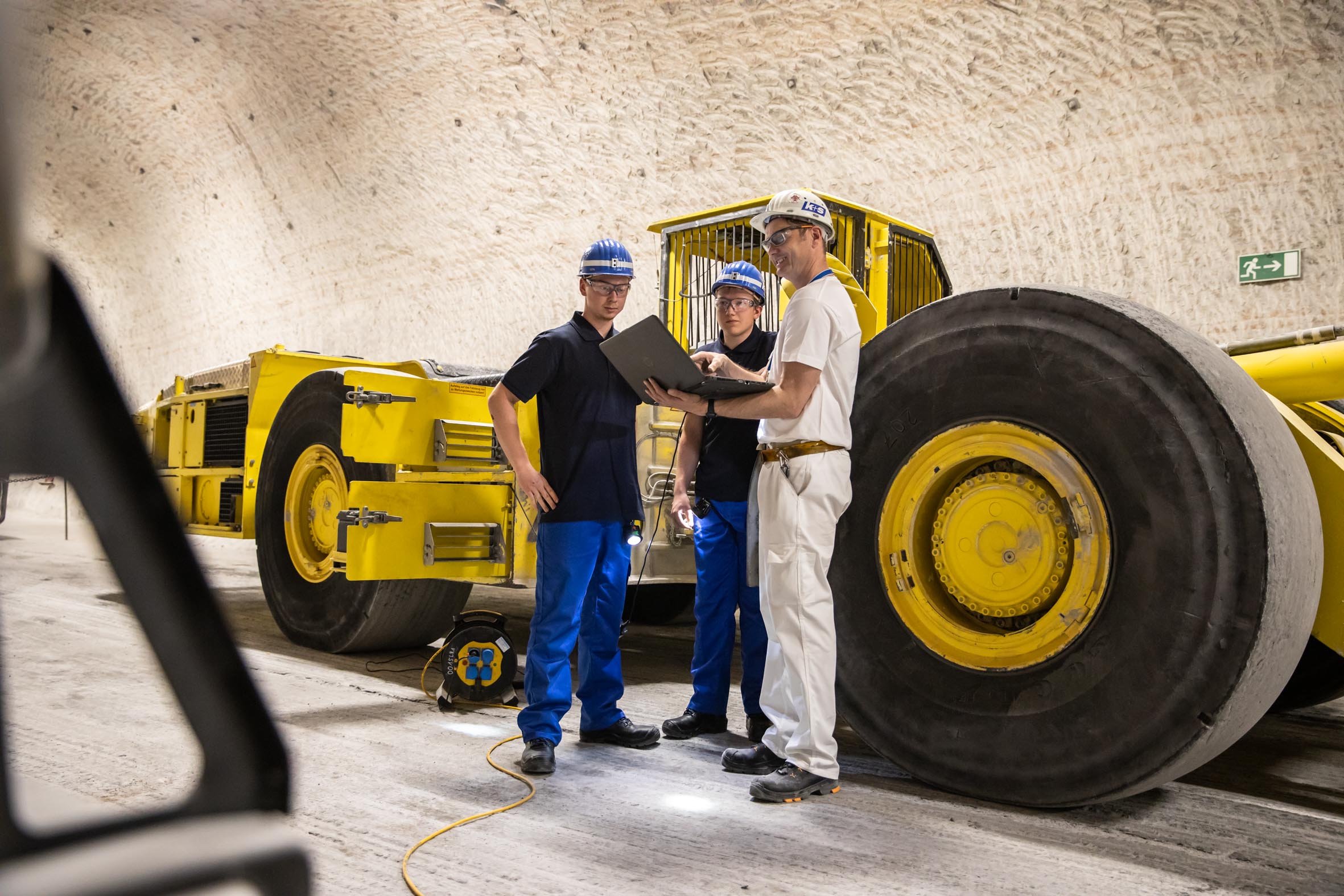 Kfz-Mechatroniker-Azubis und Ausbilder unter Tage vor großem Fahrzeug