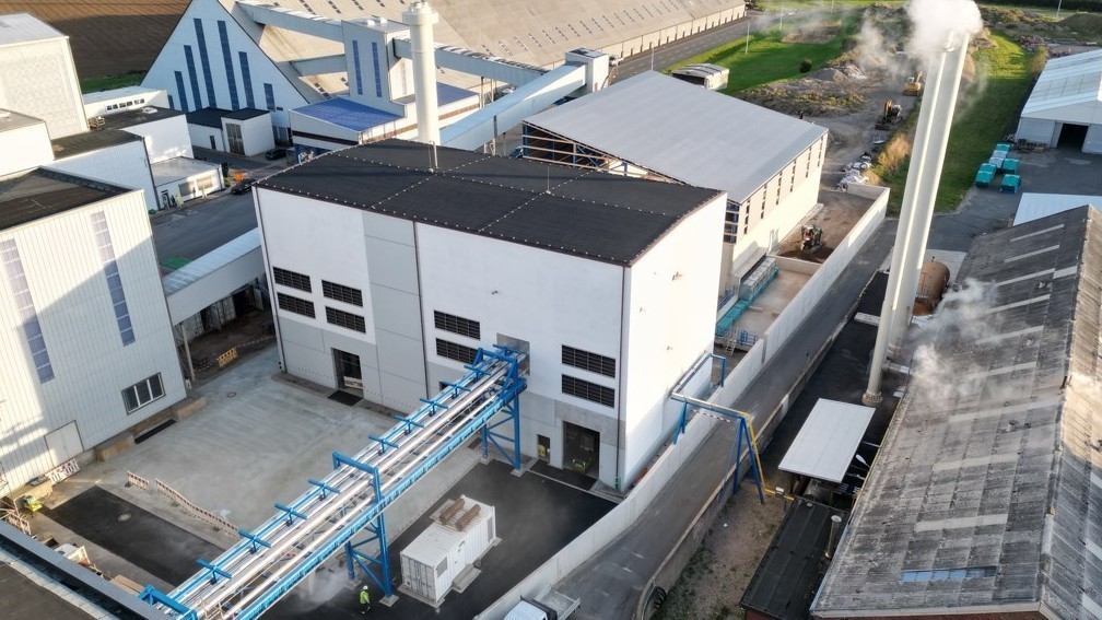 Luftaufnahme in Borth auf dem Industriekomplex von K+S mit einem großen weißen Gebäudeblock und einem angeschlossenen blauen Rohrleitungssystem. Im Hintergrund sind weitere Hallen, technische Anlagen und Grünflächen.