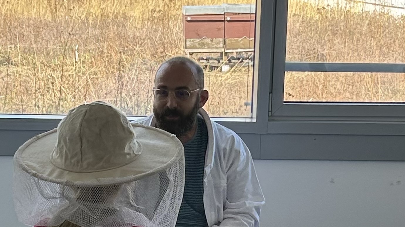 A child puts on the beekeeper's hat and the beekeeper explains its function.