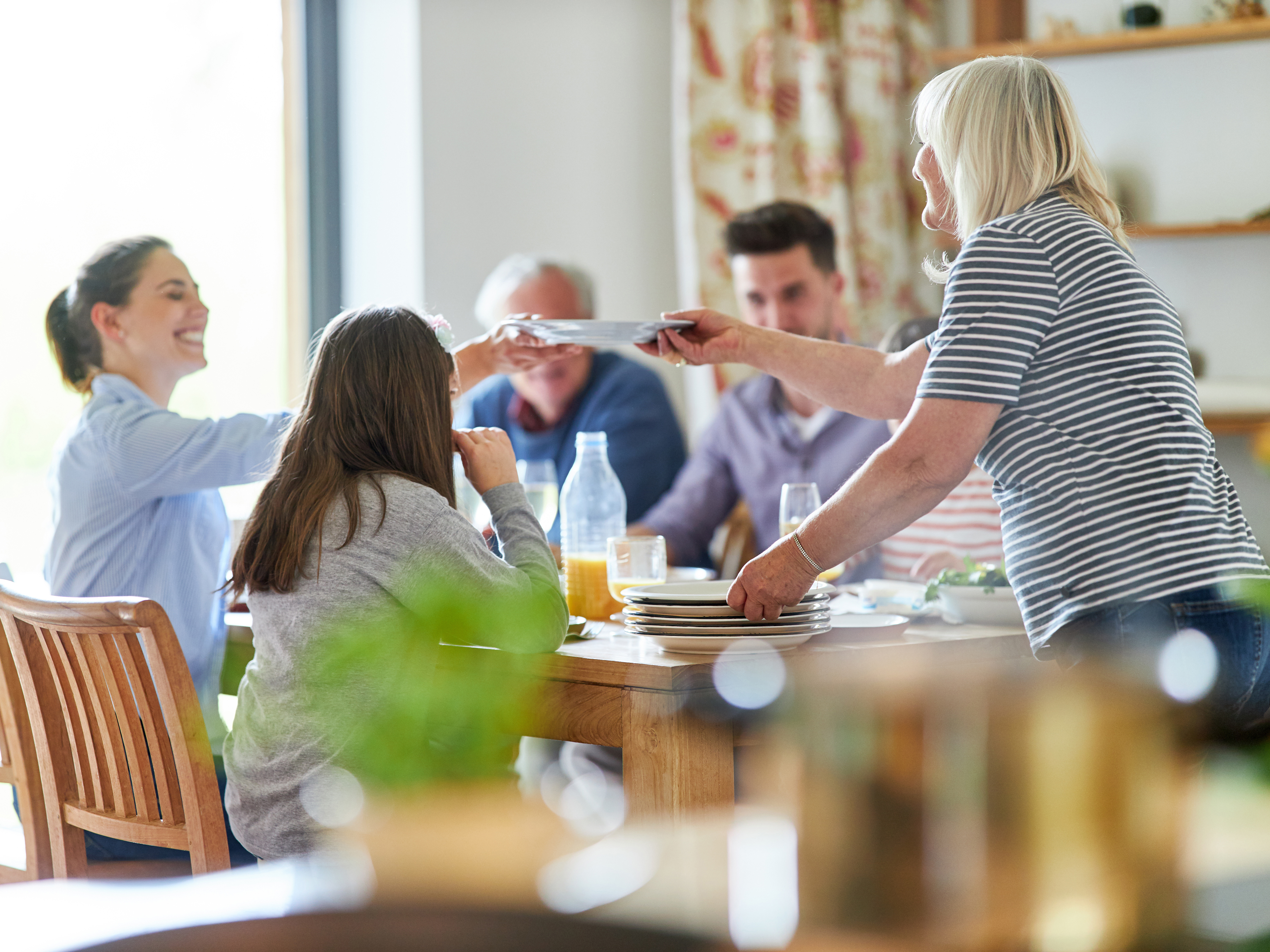 Familie sitzt am Esstisch für eine gemeinsame Mahlzeit und reicht sich strahlende Teller