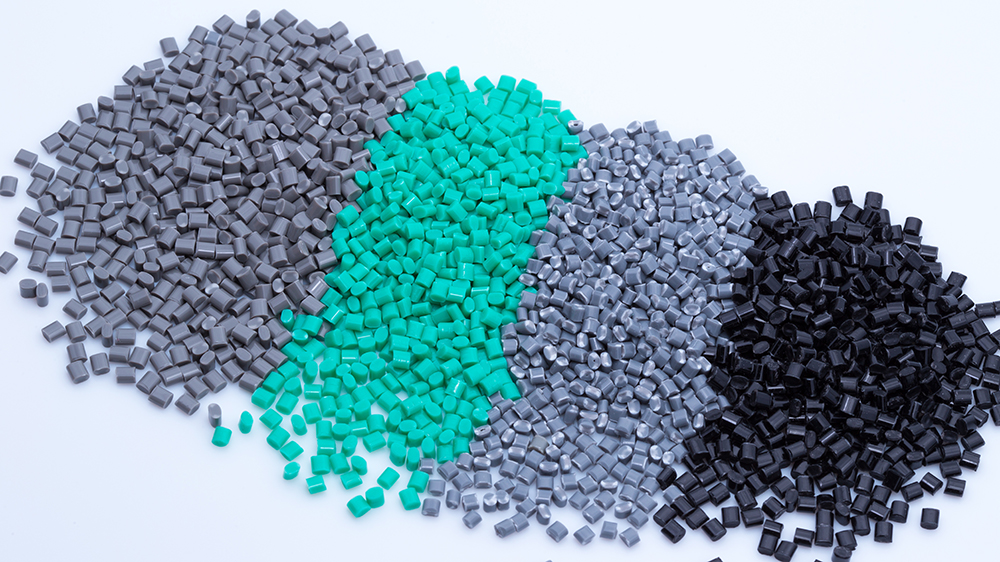 Four piles of small rectangular plastic pellets in grey, turquoise, light grey, and black on a light background, partially blending into each other