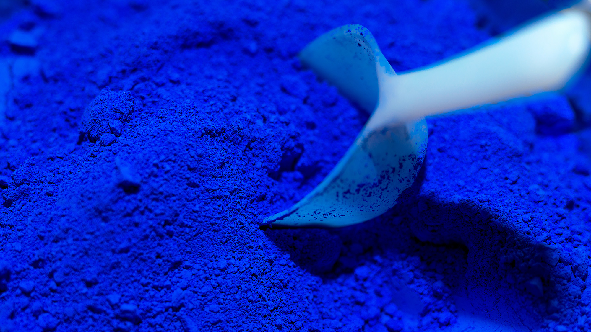 Nahaufnahme eines weissen Messloeffels in intensiv blauem Pulver