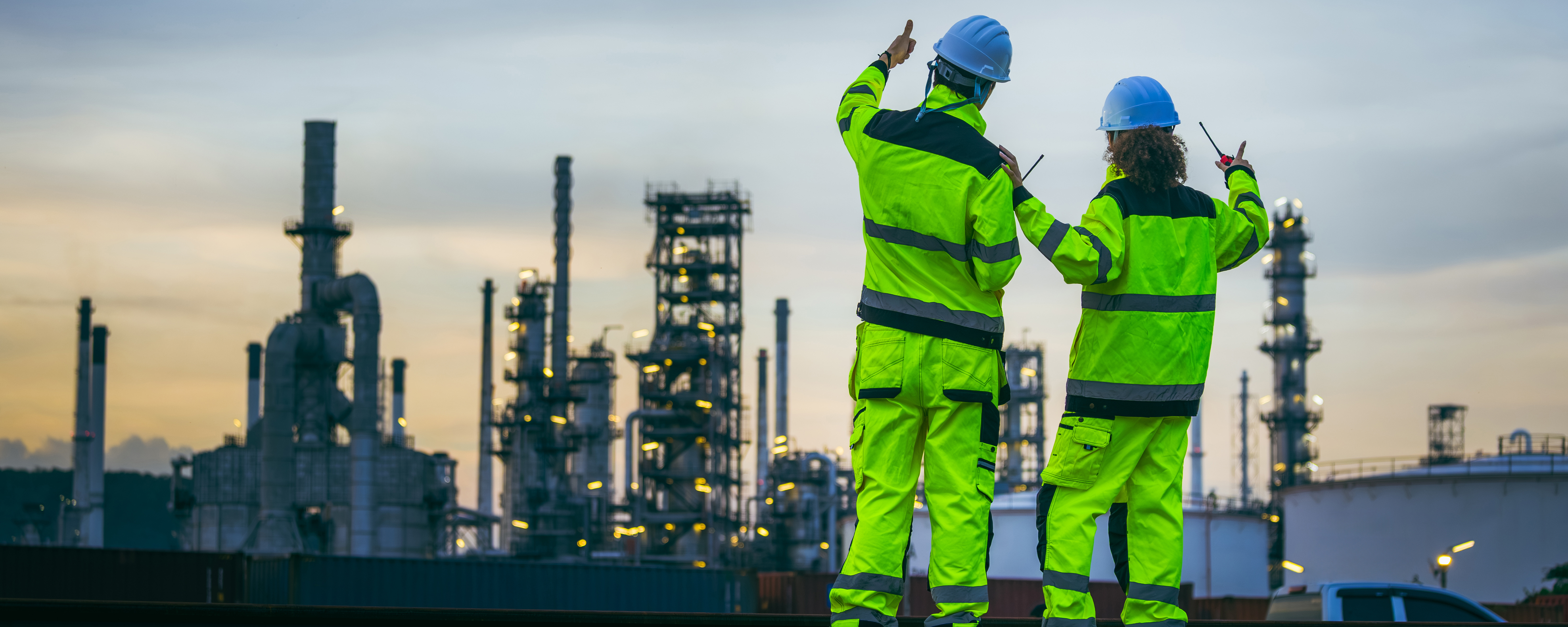 Zwei Arbeiter in Sicherheitskleidung stehen vor einer Chemianlage