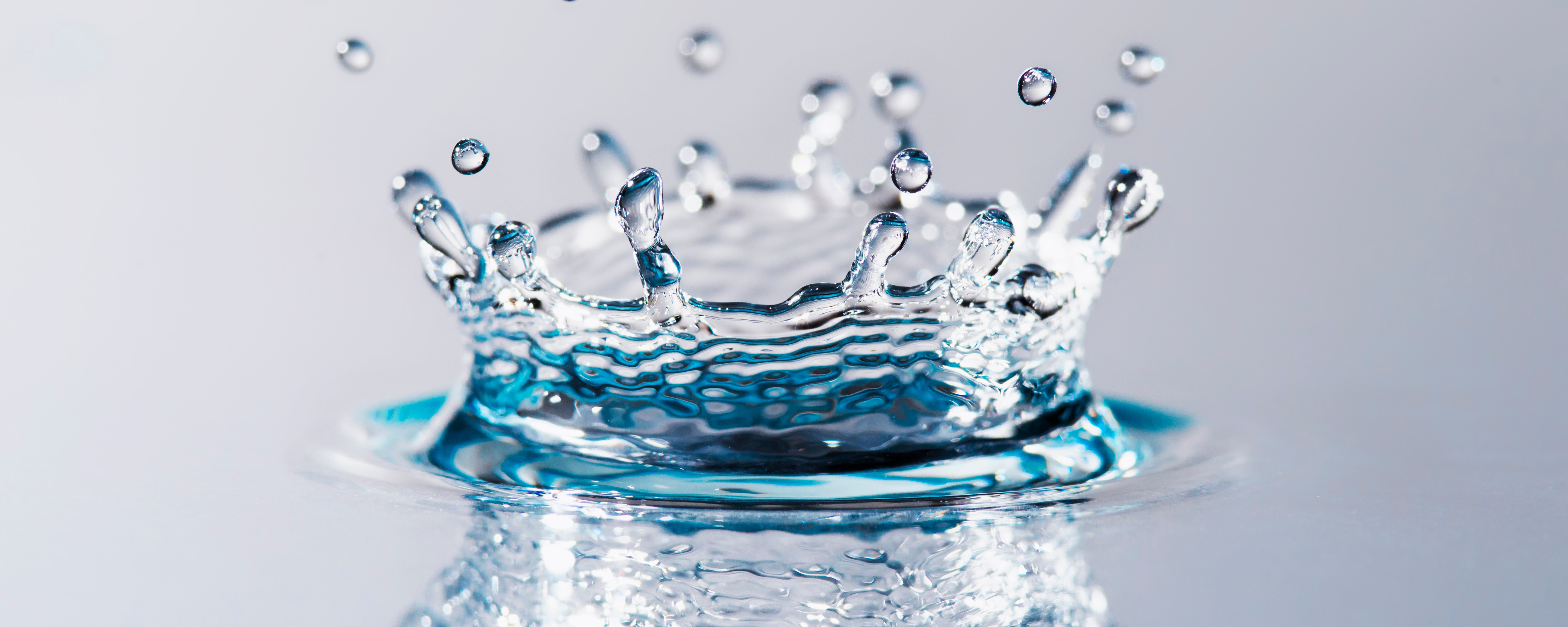 Nahaufnahme eines Wassertropfens, der auf eine Wasseroberfläche trifft und eine Krone aus Spritzern bildet.