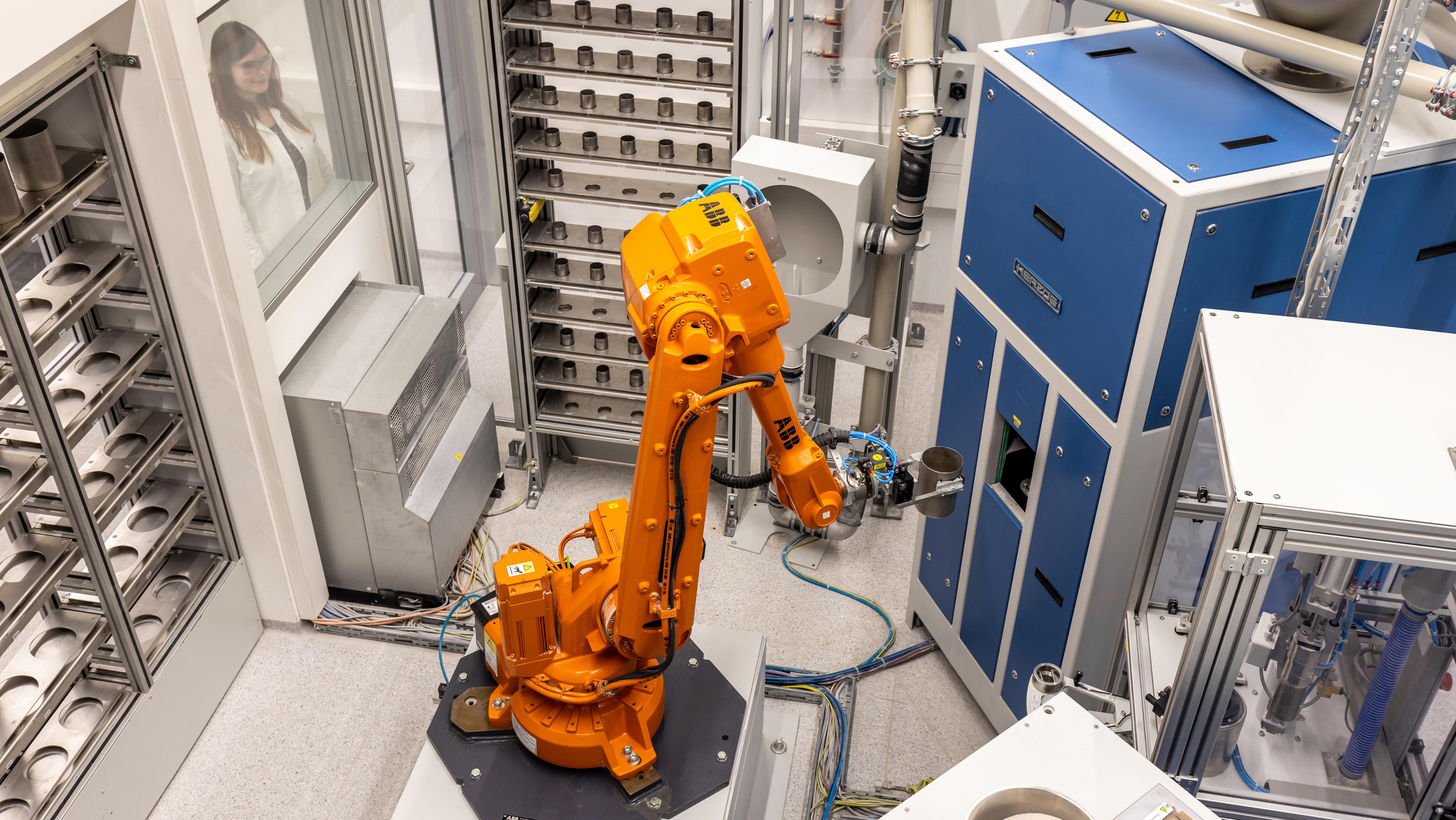 Ein oranger Roboter im Labor stellt eine Probe in einen blauen Analyseschrank.